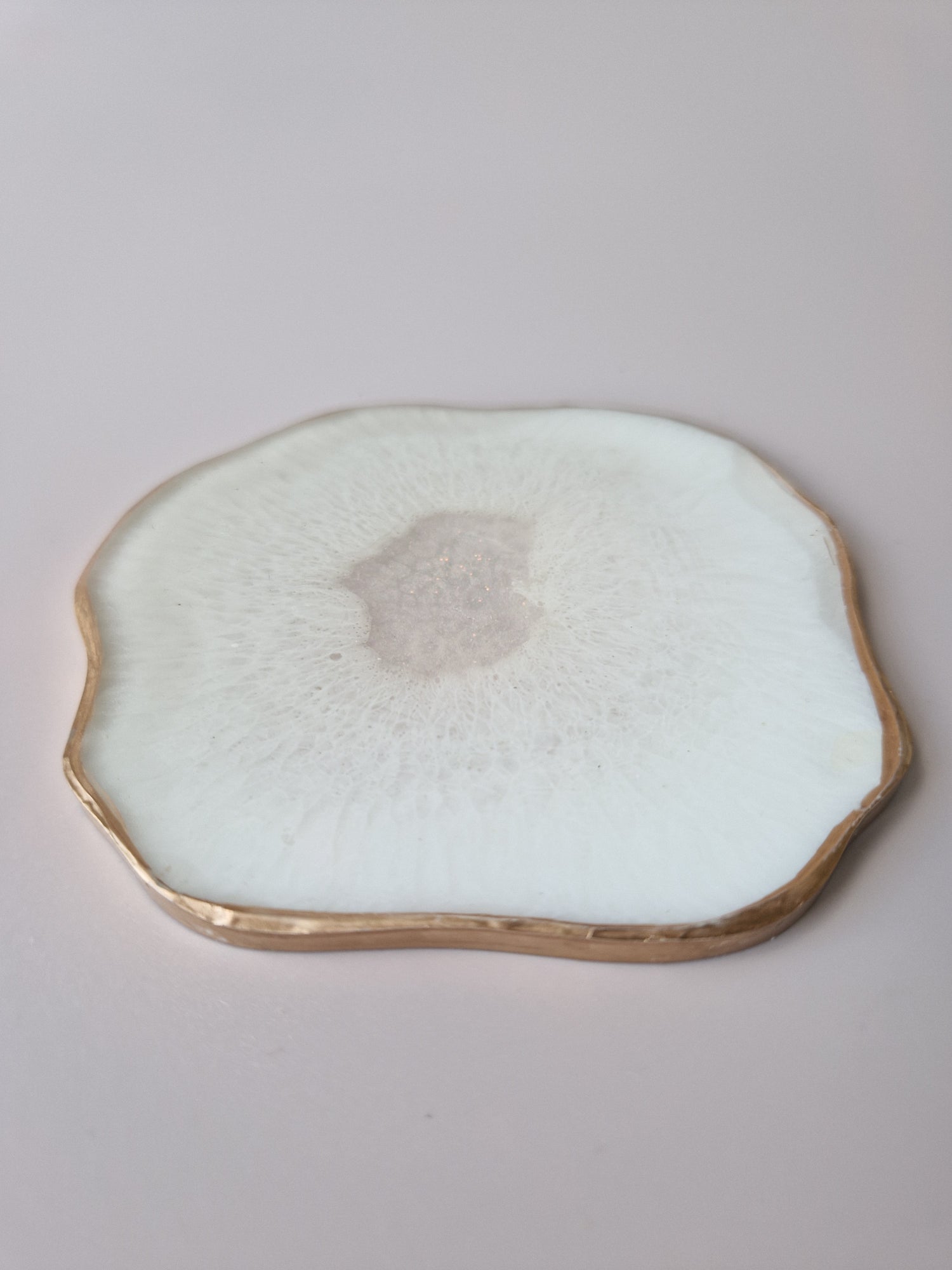 "By Hand Onderzetter Ardha, handgemaakt van epoxy in wit met subtiel glinsterend centrum en gouden rand – uniek interieuraccessoire.