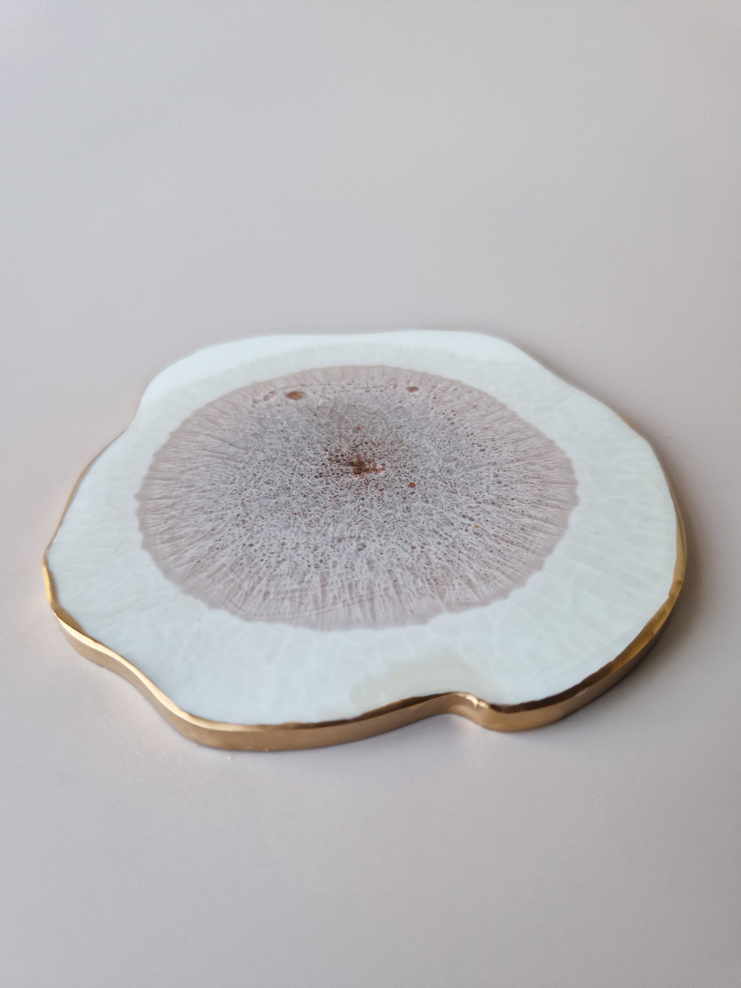 Detail van By Hand Onderzetter Erde, handgemaakt van epoxy in wit en bruin met goudkleurige rand – unieke luxe onderzetter.