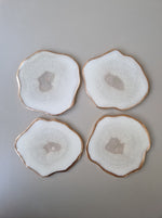 Set van vier By Hand onderzetters Ardha, handgemaakt in epoxy, wit met subtiel glinsterend centrum en gouden rand – unieke interieuraccessoires.