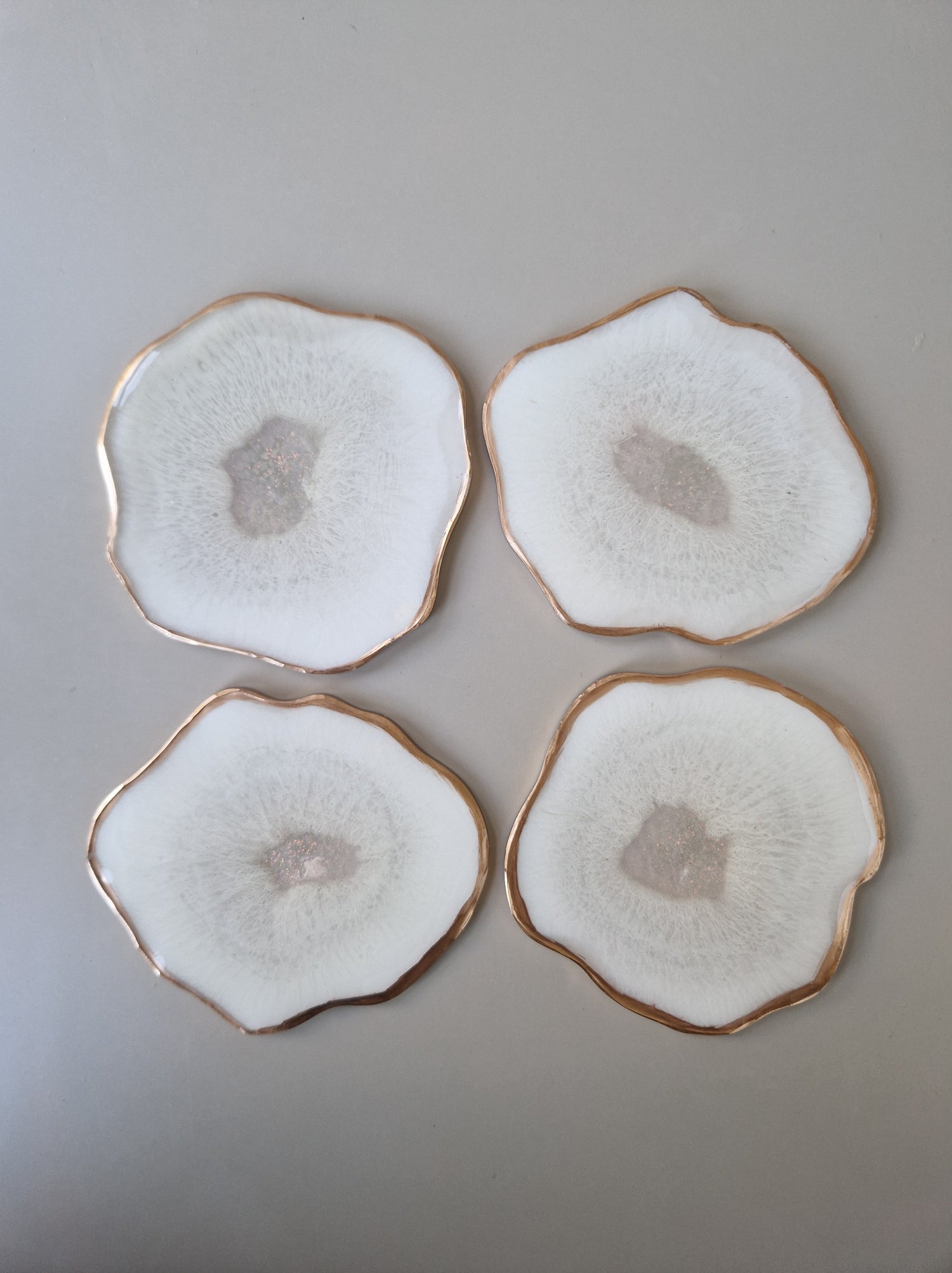 Set van vier By Hand onderzetters Ardha, handgemaakt in epoxy, wit met subtiel glinsterend centrum en gouden rand – unieke interieuraccessoires.