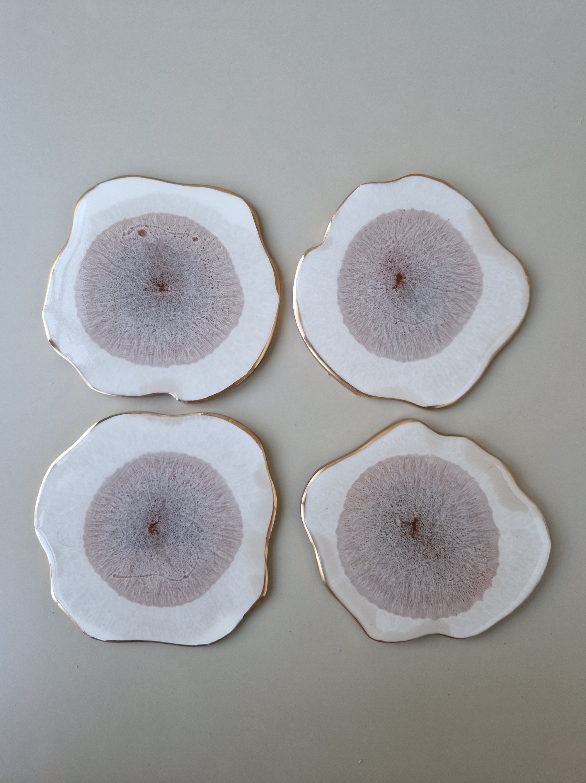 Set van vier By Hand Onderzetters Erde, handgemaakt van epoxy in wit en bruin met goudaccent – luxe handgemaakte interieuraccessoires.
