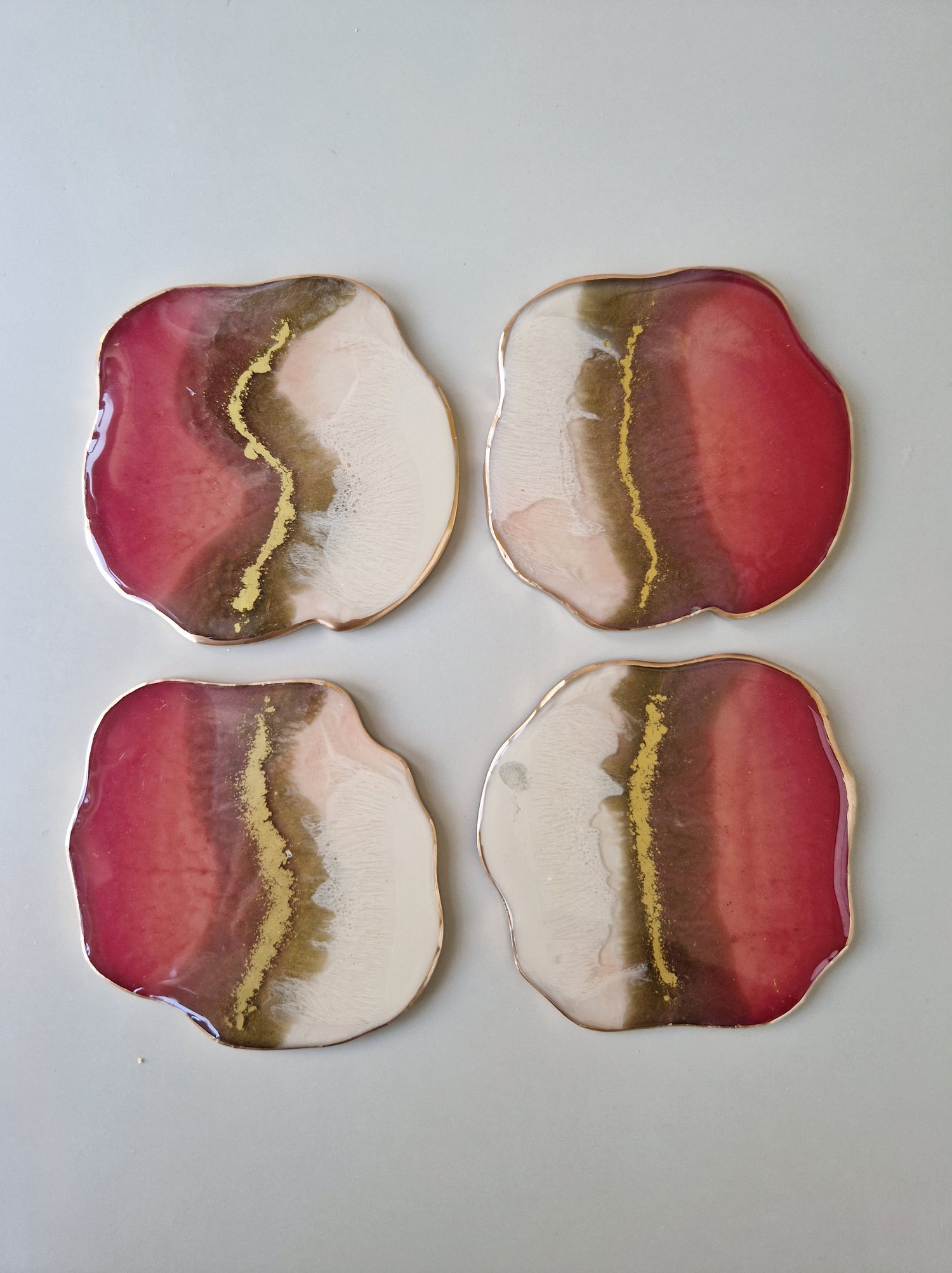 Set van vier By Hand Onderzetters Tierra, handgemaakt van epoxy in wit, roze en bruin met goudaccent – unieke luxe interieuraccessoires.